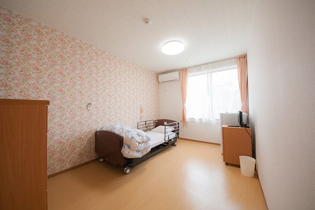 居室（全個室制）。ベッド、布団、タンス、テレビ、トイレ、洗面所などが完備しています。